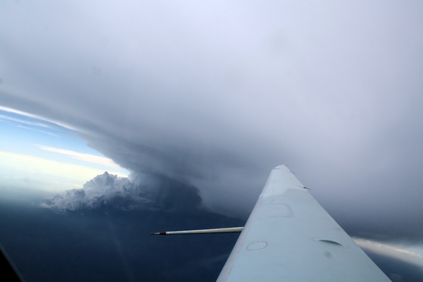 A huge anvil outflow just above the Egrett. The convective system producing the anvil can also be seen just below the wing of the aircraft.